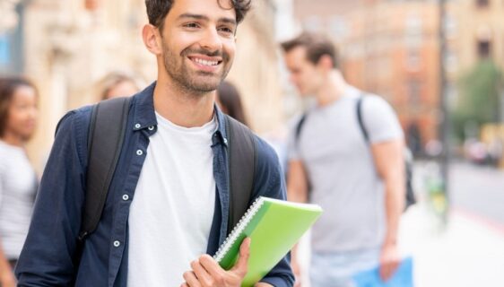 Portrait of a happy male student carrying his notebooks and smiling on the street - lifestyle concepts